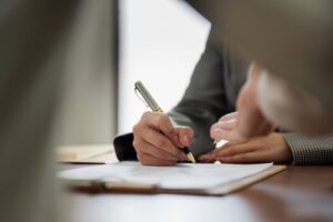 Close-up of a person signing legal documents with a pen during a meeting.