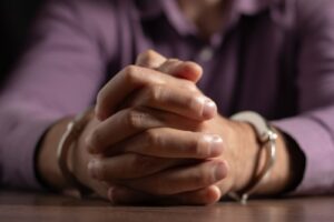 Close-up of a person in handcuffs with hands clasped together on a table.