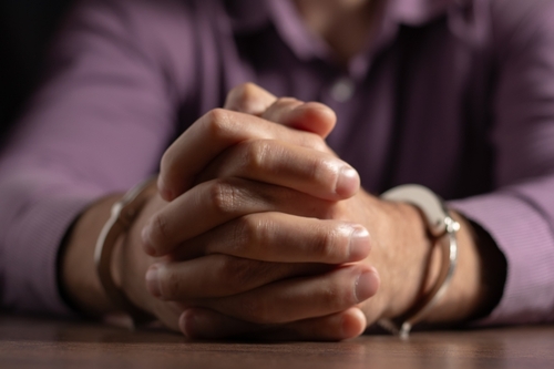 Close-up of a person in handcuffs with hands clasped together on a table.